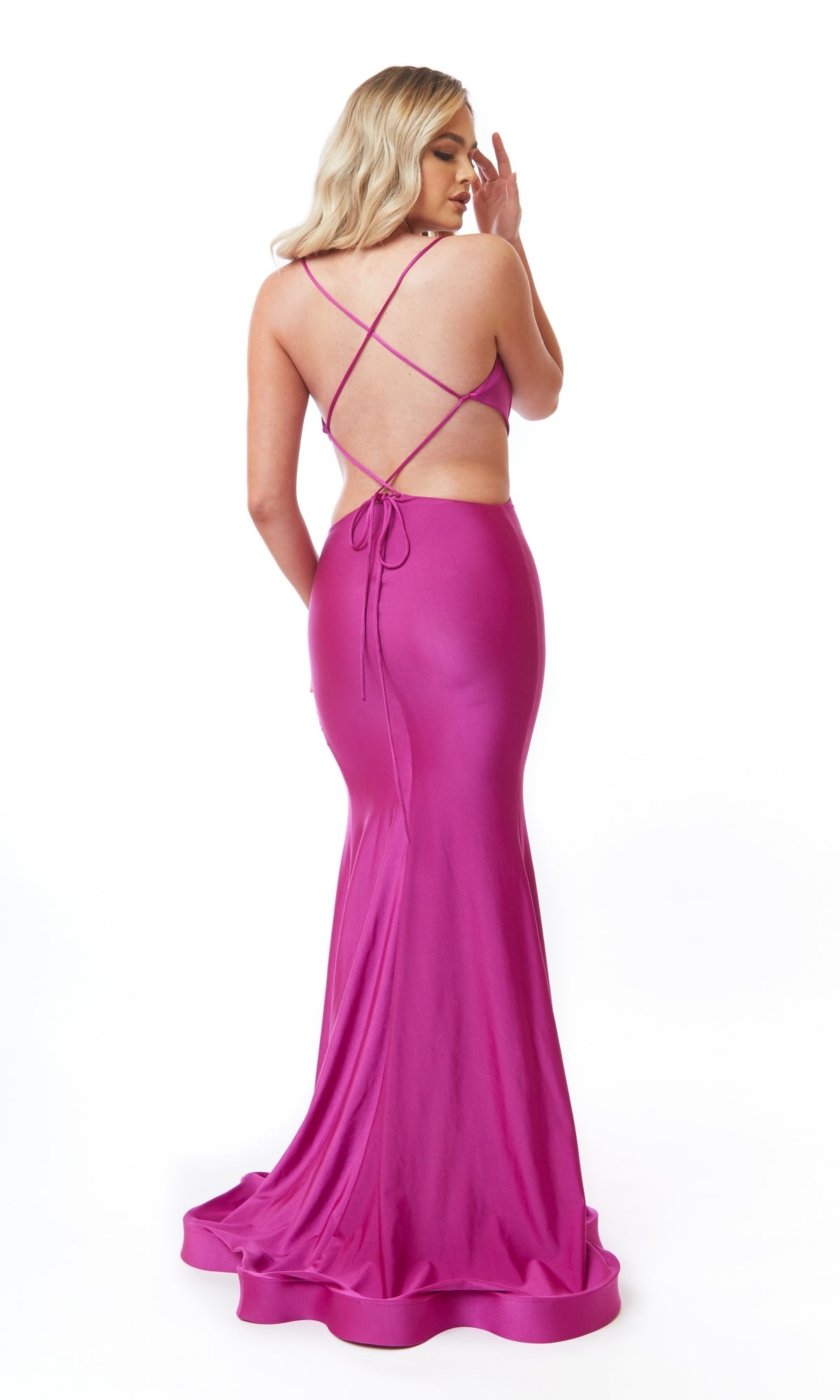 A woman wears the Sexy Long Cut-Out Prom Dress: Atria 6717H in magenta, featuring a mermaid silhouette, open back, and crisscross straps, as she stands against a plain white background.